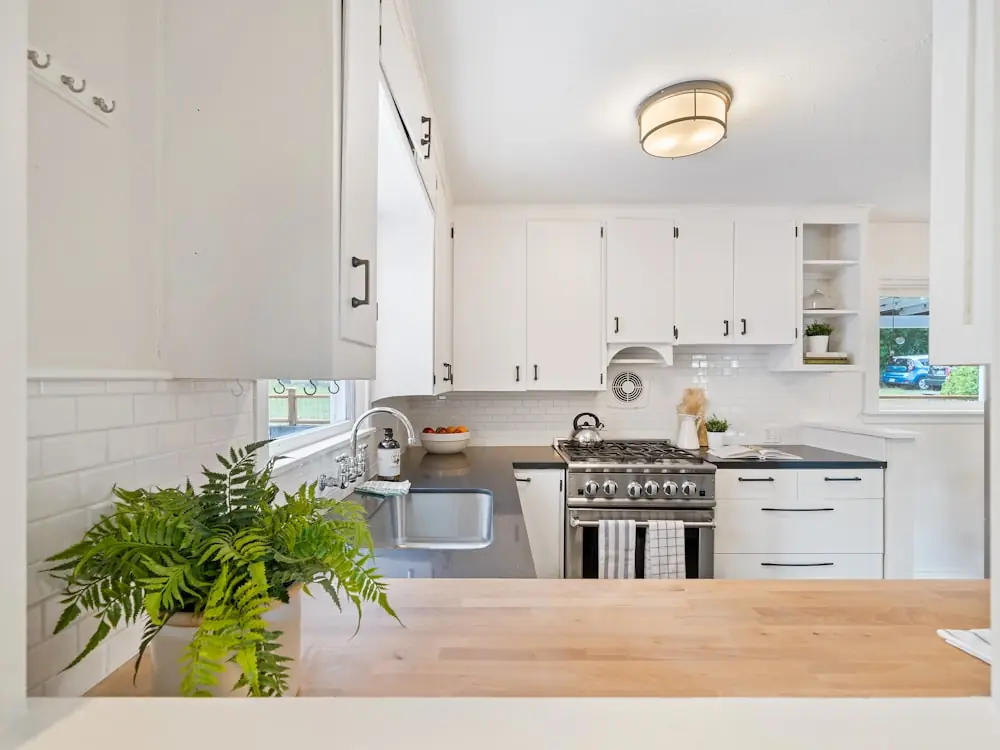 White kitchen with plants, marble counters and a bay window